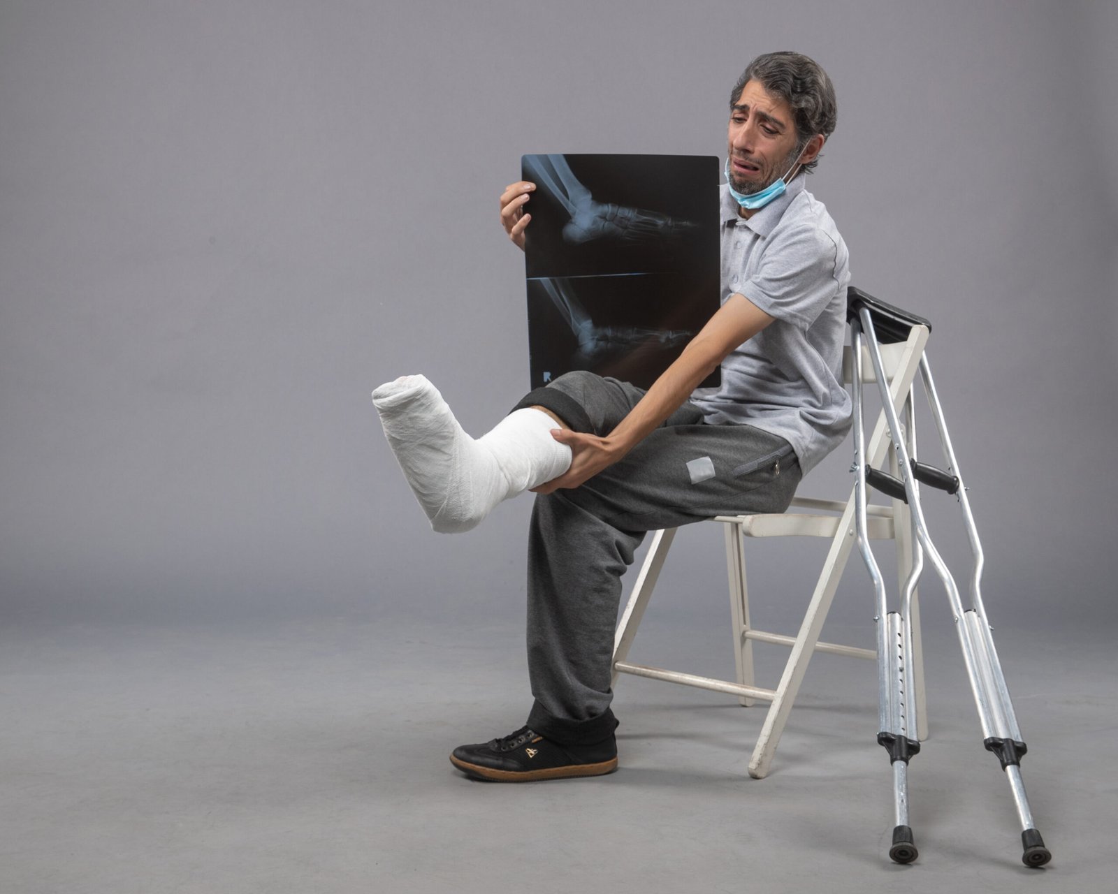 front-view-young-male-sitting-with-broken-foot-holding-x-ray-it-grey-desk-pain-leg-broken-male-accident-foot-twist